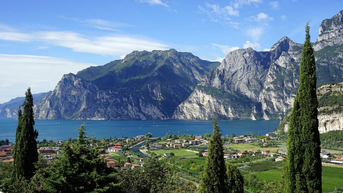 Панорама озера Гарда з селищем, кипарисами та скелястими горами під блакитним небом