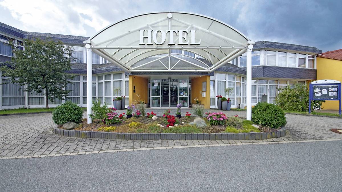 Вхід готелю з білим навісом HOTEL, клумбою квітів і скляними дверима