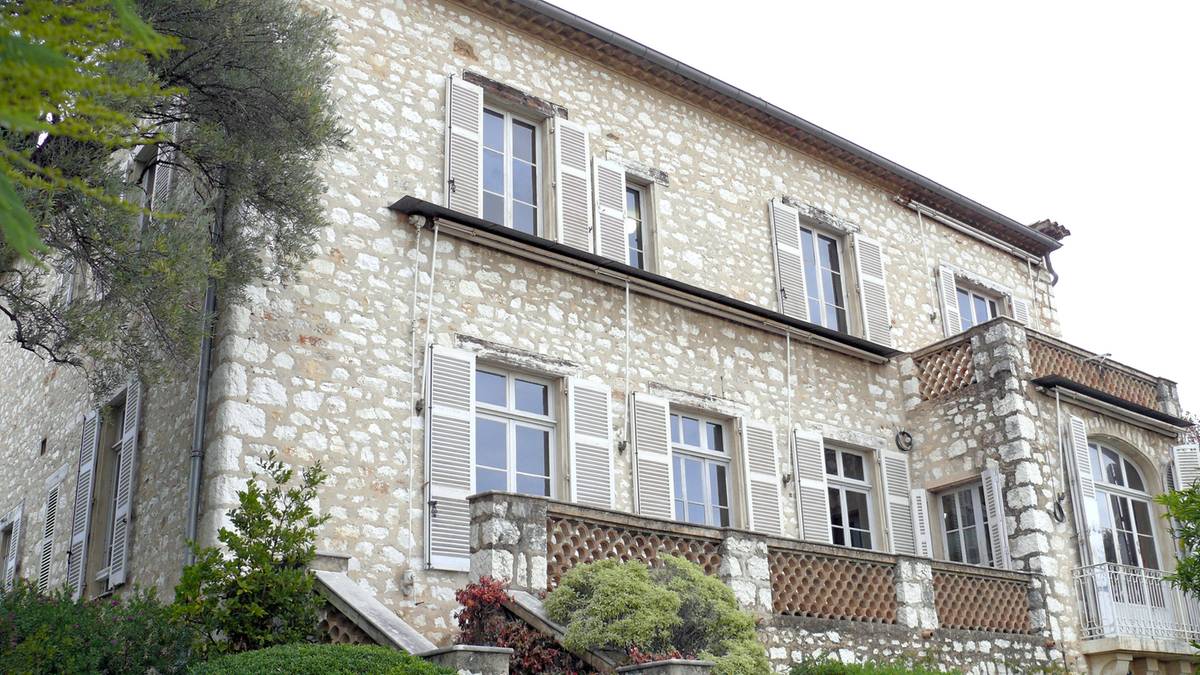 Кам’яна двоповерхова вілла з білими віконницями та балконом серед зелені